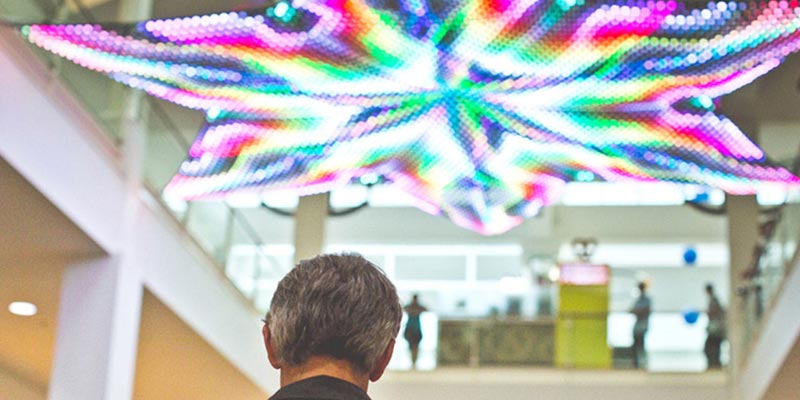 Back of a man's head on the foreground. A colorful star-shaped LED installation hanging in the background.