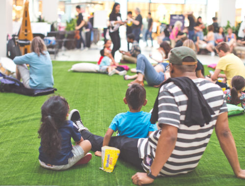 Man and two kids sitting on the fake grass looking on the LED Constellation