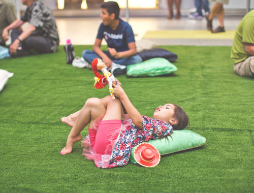 Little girl lying on the fake grass and a pillow looking up the LED Constellation