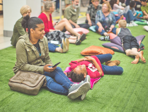 Woman sitting on the fake grass and the boy lying on the grass under the LED Constellation